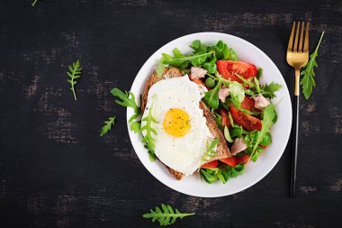 Kahvaltı - kızarmış yumurtalı tost ve yeşillikli domates salatası ve koyu arkaplanda morina ciğeri. Sağlıklı kahvaltı. Üst görünüm