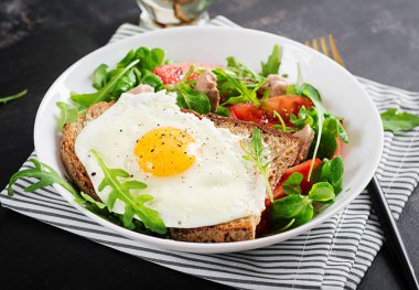 Kahvaltı - kızarmış yumurtalı tost ve yeşillikli domates salatası ve koyu arkaplanda morina ciğeri. Sağlıklı kahvaltı..