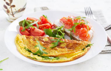 Kahvaltıda. Peynirli omlet, yeşil roka ve beyaz tabakta somonlu sandviç. Frittata - İtalyan omleti.