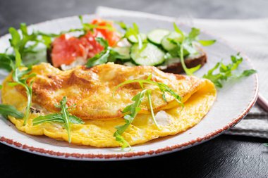 Kahvaltıda. Peynirli omlet, somon balıklı sandviç ve beyaz tabakta salatalık. Frittata - İtalyan omleti.