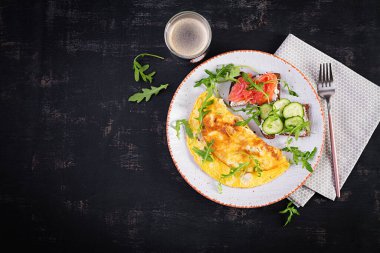 Kahvaltıda. Peynirli omlet, somon balıklı sandviç ve beyaz tabakta salatalık. Frittata - İtalyan omleti. Üst görünüm
