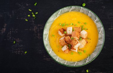 Creamy pumpkin puree soup with croutons, peppers and green onions. Top view, above