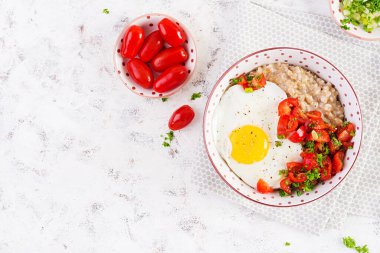 Breakfast oatmeal porridge with roasted egg and tomatoes salad. Healthy balanced food. Top view, above