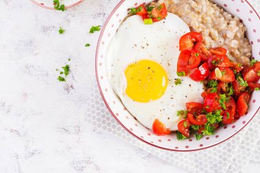 Breakfast oatmeal porridge with roasted egg and tomatoes salad. Healthy balanced food. Top view, above
