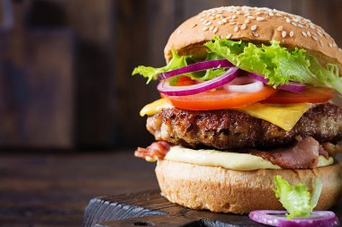 Hamburger with bacon, turkey burger meat, cheese, tomato and lettuce on wooden background. Tasty burger. Close up