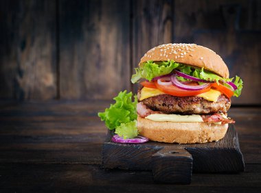 Hamburger with bacon, turkey burger meat, cheese, tomato and lettuce on wooden background. Tasty burger. Close up