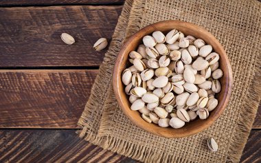 Pistachio nuts in shell  in bowl on wooden background. Top view, overhead
