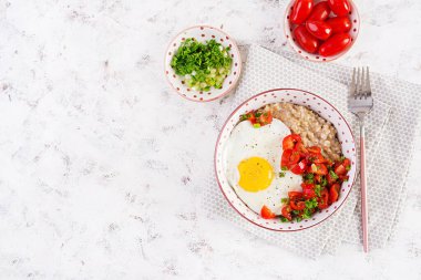 Breakfast oatmeal porridge with roasted egg and tomatoes salad. Healthy balanced food. Top view, above