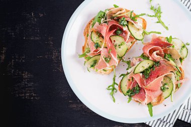 Kahvaltı ya da brunch. Prosciutto ya da jamonlu sandviçi beyaz tabakta aç. Akdeniz aperatifi. Üst görünüm, genel görünüm