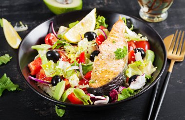 Fırında somon balığı fileto ve taze yeşil marul, domates, avokado ve siyah zeytin. Yunan salatası.