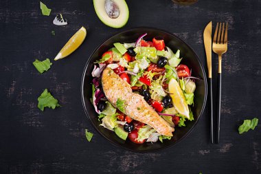 Fırında somon balığı fileto ve taze yeşil marul, domates, avokado ve siyah zeytin. Yunan salatası. Üst görünüm.