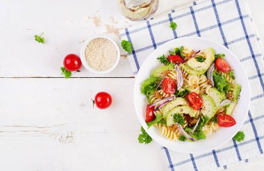 Avokado, domates, taze yeşil marul, beyaz arka planda kırmızı soğan ve hardal soslu Fusilli makarna salatası. Vejetaryen sağlıklı öğle yemeği. Üst manzara, düz uzanma
