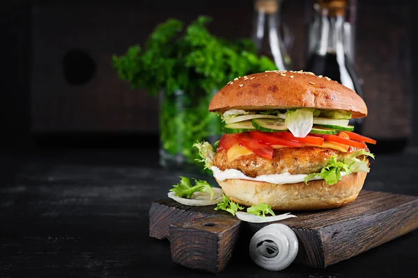 Hamburger with chicken burger meat, cheese, tomato, cucumber and lettuce on wooden background. Tasty burger. Close up