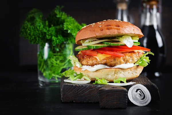 Hamburger with chicken burger meat, cheese, tomato, cucumber and lettuce on wooden background. Tasty burger. Close up