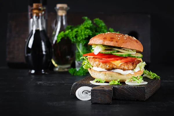 Hamburger with chicken burger meat, cheese, tomato, cucumber and lettuce on wooden background. Tasty burger. Close up