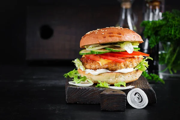 Hamburger with chicken burger meat, cheese, tomato, cucumber and lettuce on wooden background. Tasty burger. Close up