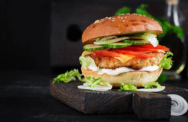 Hamburger with chicken burger meat, cheese, tomato, cucumber and lettuce on wooden background. Tasty burger. Close up