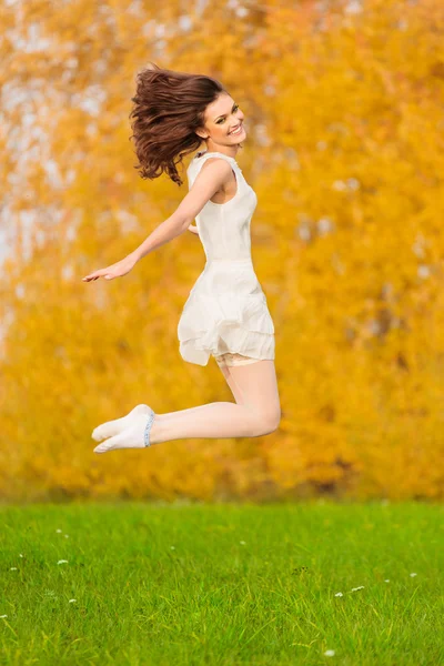 美丽的年轻女孩在跳的背景上的白色礼服 — 图库照片