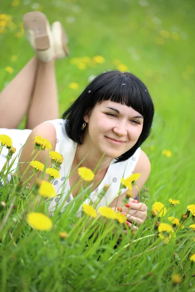 Young woman lying on grass in the field of dandelion — Stock Photo, Image