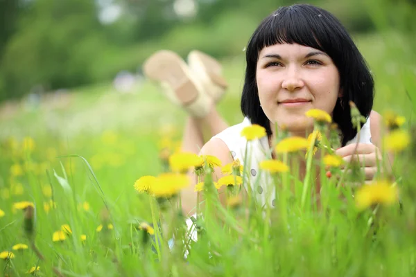 Young woman lying on grass in the field of dandelion — Stock Photo, Image