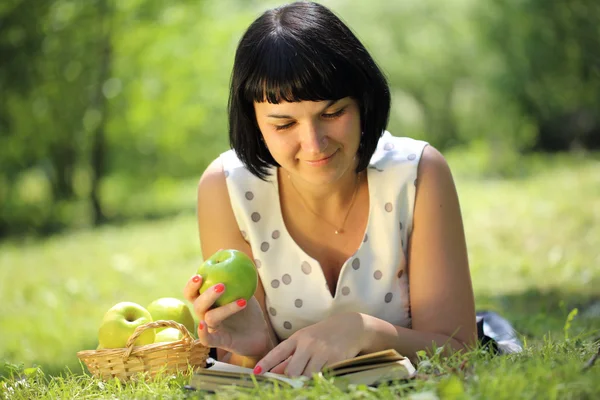 Молода жінка тримає яблуко і читає книгу на траві — стокове фото