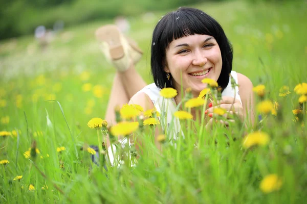 Young woman lying on grass in the field of dandelion — Stock Photo, Image