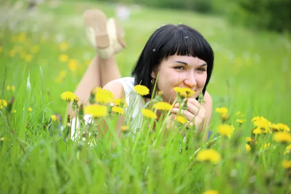 Young woman lying on grass in the field of dandelion — Stock Photo, Image