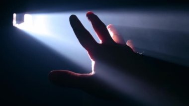 Elini ışık huzmesine karşı tutan adam.