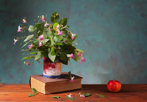 Flowers in a vase on a book and an apple — Stock Photo, Image
