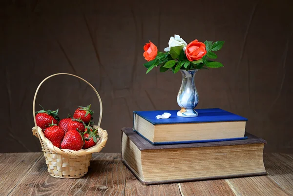 Verse aardbeien in een rieten mand en bloemen in een vaas — Stockfoto