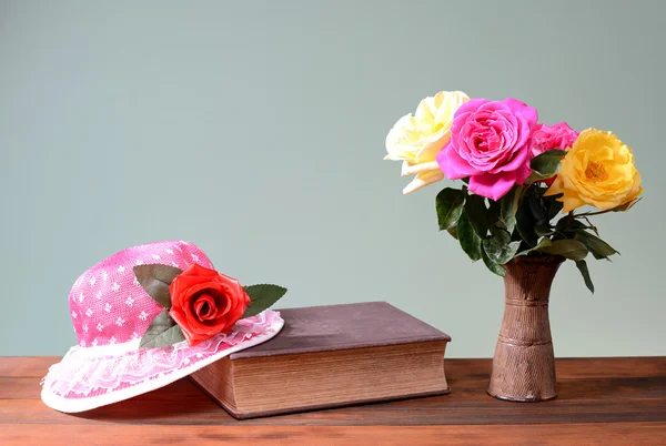 Rosor i keramik vas, en bok och en hatt — Stockfoto