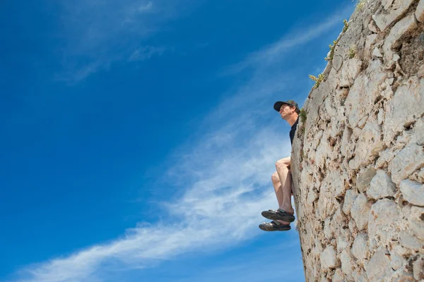 Jonge man zit op de rand van de muur — Stockfoto