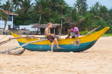 turist ve plajda bir geleneksel sri Lankalı Balıkçı teknesinde oturan yerel adam