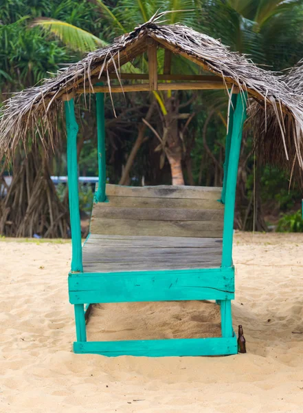 Cama de sol turquesa vazia coberta com folhas de palmeira na praia de areia . — Fotografia de Stock