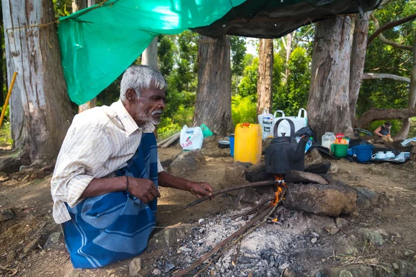 Homem local idoso fervendo água em uma panela no fogo do acampamento na floresta . — Fotografia de Stock