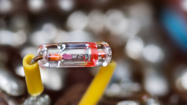 Closeup of old germanium point-contact diode in sealed glass tube. Retro electrical component in transparent package with two yellow insulated wires on a blurry background with white bokeh. Electronics.