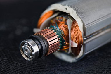 Rotor and stator detail of electric DC motor on a black mesh background. Closeup of steel ball bearing, copper commutator or coil wires inside metal laminations of drill machine engine on dark blue net.