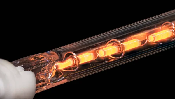 Glowing coiled resistance wire inside heating element on a black background. Closeup of orange hot metal conductor in vacuum glass tube. Conversion electric energy into heat in laser printer finisher.