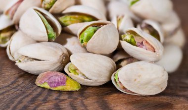 Kapalı kabuklu yeşil çekirdekli kavrulmuş şam fıstığı. Pistacia vera. Kahverengi ahşap üzerine tuzlu aromalı şam fıstığı istifi. Proteinli ve sağlıklı vitaminli lezzetli yiyecekler..