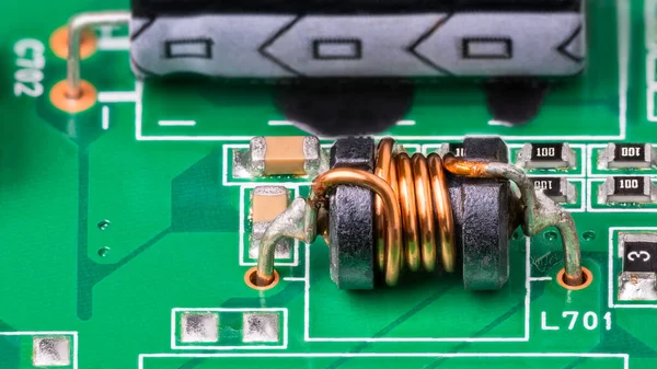 Green PCB detail with electromagnetic coil and electronic surface-mount components. Close-up of small inductor with copper wire on ferrite core, electrolytic capacitor and resistors. Electrotechnics.