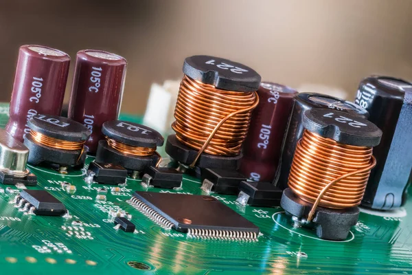 Closeup of electromagnetic coils and electrolytic capacitors or chips on a green PCB. Various electrical components on printed circuit board with surface-mounted devices. Electronic cylindric inductors.