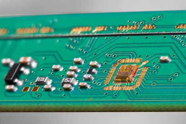 Gold wires of chip bonding to green PCB detail from flatbed scanner on a gray background. Integrated circuit die wired to electronic printed board with surface mounted components and line scan camera.