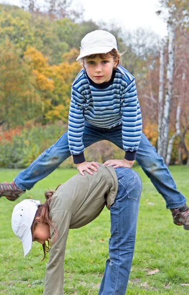 Niño saltando sobre la chica en el parque de otoño en una hierba — Foto de Stock