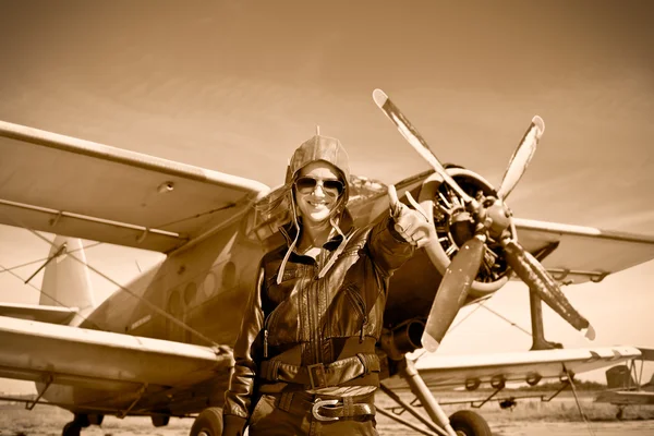 Portrait of beautiful female pilot with plane behind.