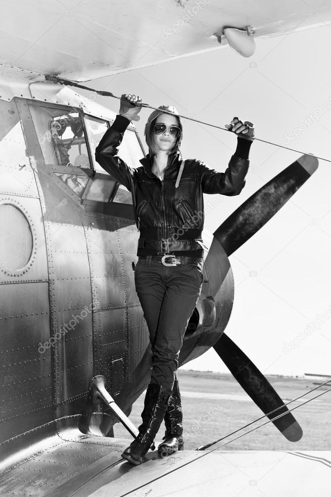 Beautiful girl in black jacket standing on a war aircraft.