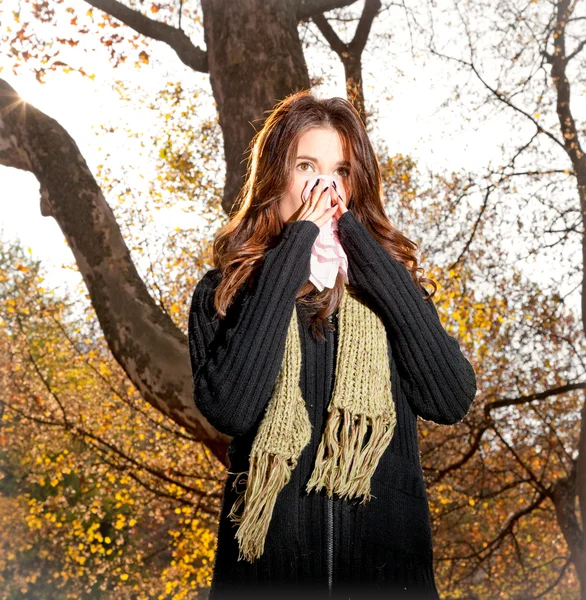 Caucasian woman with cold sneezing into tissue in park — Stock Photo, Image