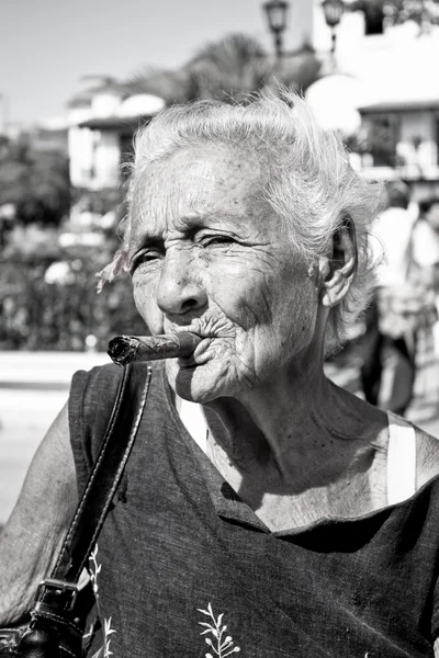 Vieja mujer arrugada con cigarro humeante de flor roja. Cuba — Foto de Stock