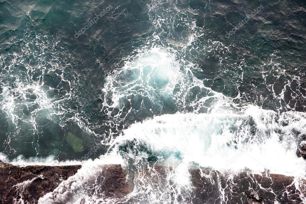 Sea wave breaking against coast cliff