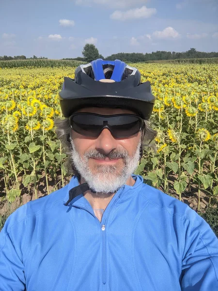 Ώριμος Ποδηλάτης Φορώντας Κράνος Μπροστά Από Πεδίο Ηλιοτρόπιο — Φωτογραφία Αρχείου