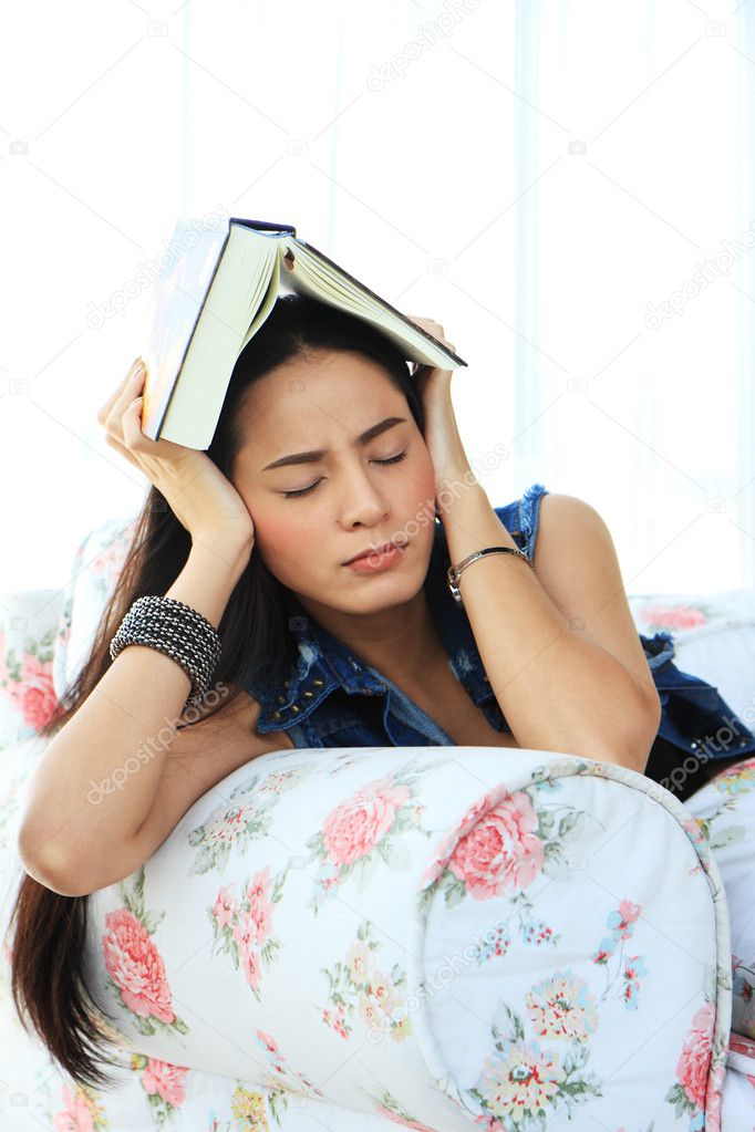 Tired young woman taking a nap at home lying on sofa with a book